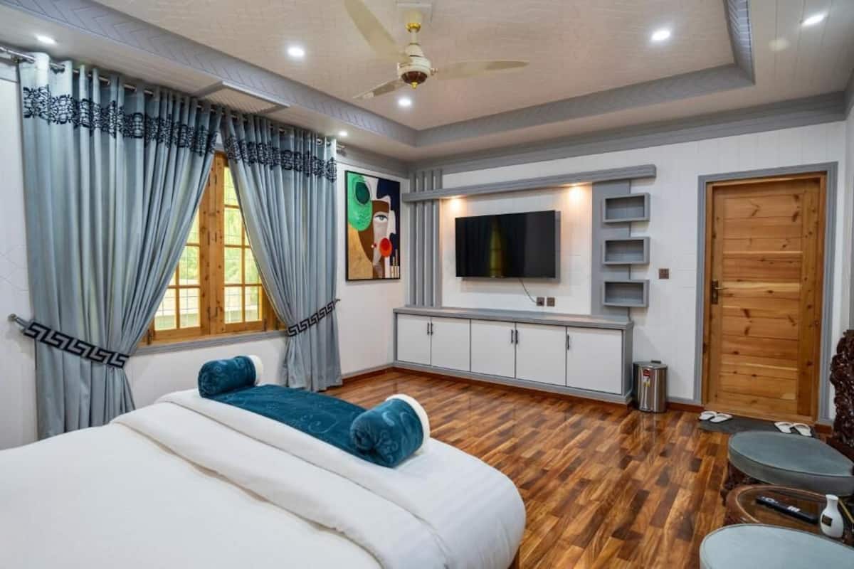 Un dormitorio moderno con cama, cortinas, televisor y puerta de madera.