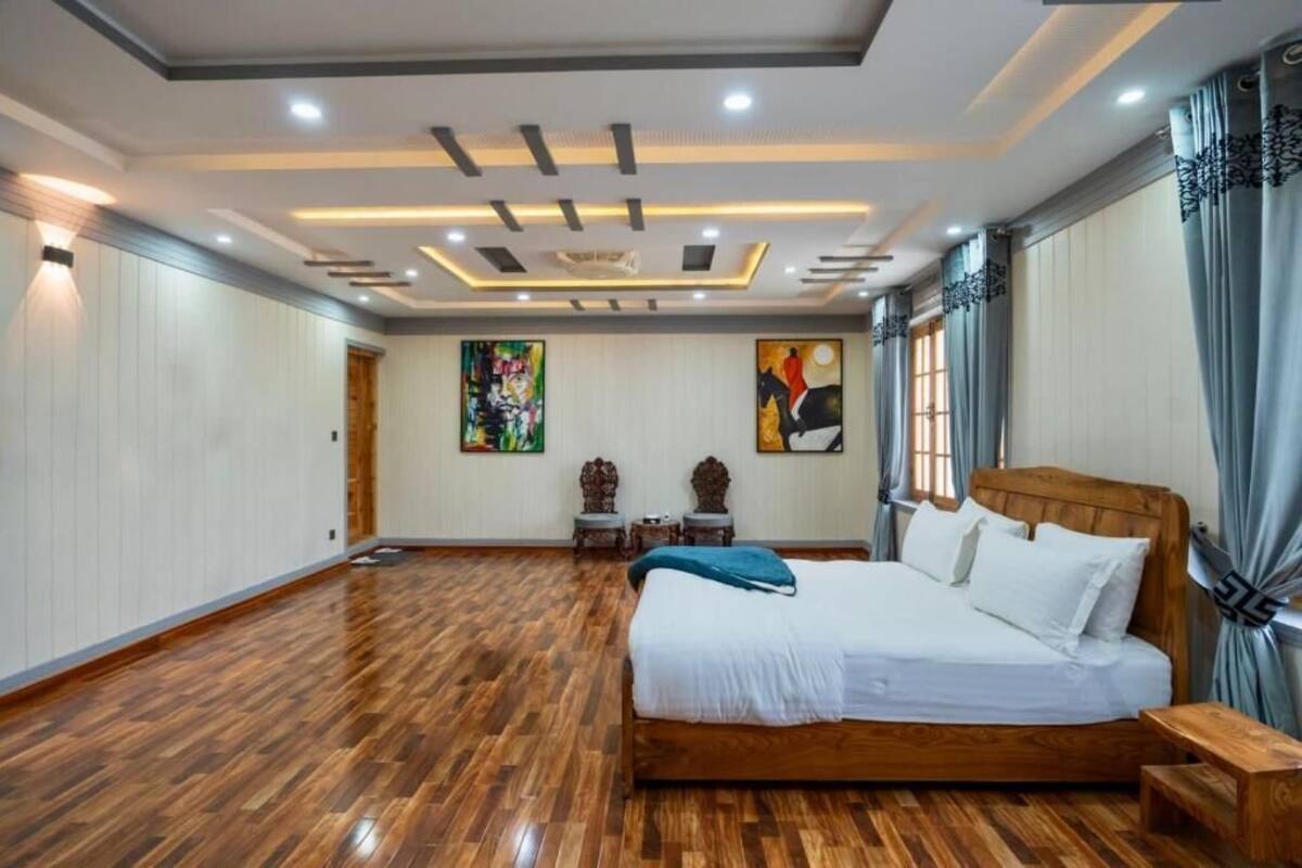 Un dormitorio amplio con una cama grande, suelo de madera y un diseño de techo moderno.