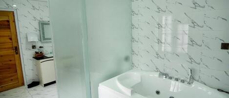 A modern bathroom with a large bathtub, a glass shower enclosure, and marble-patterned walls.