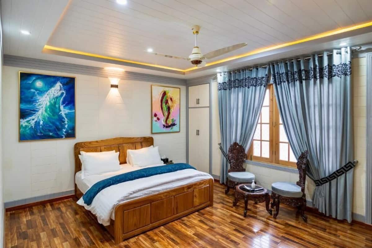 Un dormitorio con una cama de madera, un ventilador de techo, un cuadro de noche estrellada, un cuadro abstracto colorido y una ventana con cortinas.