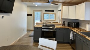 A modern kitchen with wooden ceiling, built-in appliances, and a large window.