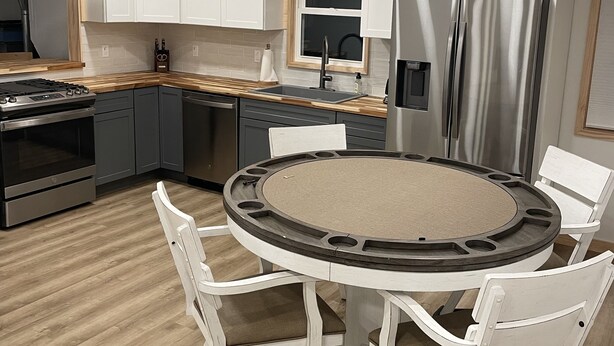 A modern kitchen with white cabinets, a stainless steel refrigerator, a round dining table with white chairs, and a ceiling fan.