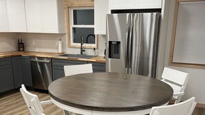 A modern kitchen with white cabinets, a stainless steel refrigerator, and a round dining table with white chairs.