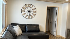 A modern living room with a sectional sofa, a wooden ceiling with recessed lighting, and a wall clock.