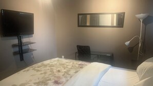 A hotel room with a bed, a TV mounted on the wall, a desk with a chair, and a floor lamp. - Cozy Luxury in peaceful Caledonia,  13 minutes away from Hamilton Airport  (Caledonia)
