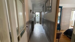 A narrow hallway with a wooden floor, leading to a room with a bed and a chair.