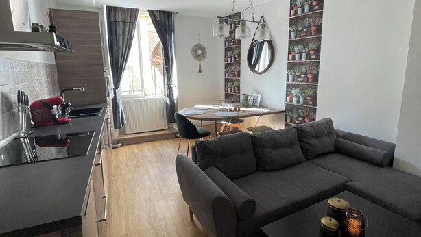 A modern living space with a kitchen, dining area, and a large grey sofa.