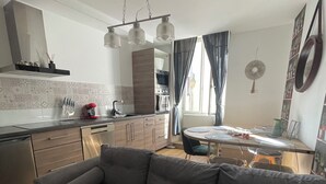 A modern living room with a grey sofa, a dining table, and a kitchen in the background.