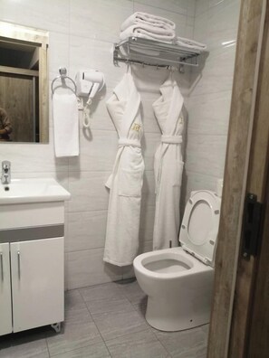 A bathroom with a white sink, a toilet, and two white robes hanging on hooks.