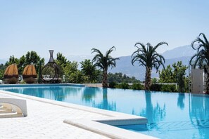 A swimming pool with clear blue water, surrounded by palm trees and a mountain view.