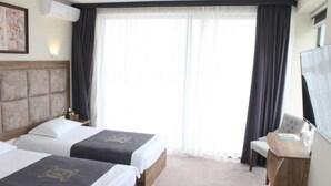 Ein Hotelzimmer mit zwei Betten, einem Schreibtisch, einem Sessel, einem Fernseher und einem großen Fenster mit Vorhängen.