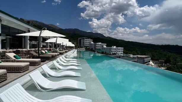 Ein Poolbereich mit Liegestühlen und Sonnenschirmen, ein gefliester Weg und ein Blick auf Berge unter einem teils bewölkten Himmel.