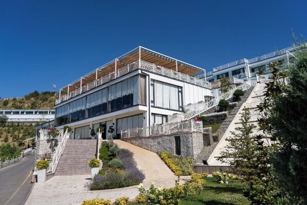 A modern building with a prominent staircase leading to a covered upper level, surrounded by landscaped gardens and a clear view of the surrounding landscape.