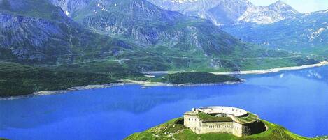 A castle on a hill overlooking a lake with mountains in the background.
