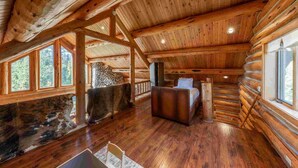A log cabin interior with a stone fireplace, wooden beams, a sofa, and large windows. - Old Trail Hideaway: 3  BR, 2  BA House in Wilson, Sleeps 9 (Wilson)
