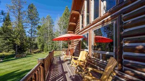 A wooden deck with rocking chairs and a red umbrella, overlooking a well-maintained lawn and trees. - Old Trail Hideaway: 3  BR, 2  BA House in Wilson, Sleeps 9 (Wilson)