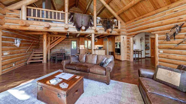 A spacious log cabin with a high ceiling, a central living area with a leather sofa, a wooden coffee table, and a rustic staircase. - Old Trail Hideaway: 3  BR, 2  BA House in Wilson, Sleeps 9 (Wilson)