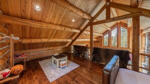 A log cabin interior with wooden beams, a loft bed, a small table, and a basketball. - Old Trail Hideaway: 3  BR, 2  BA House in Wilson, Sleeps 9 (Wilson)