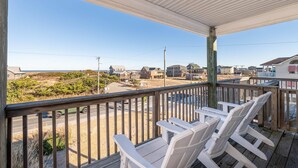 Un espace extérieur abrité, doté de chaises en bois et offrant une vue sur une plage et des maisons.