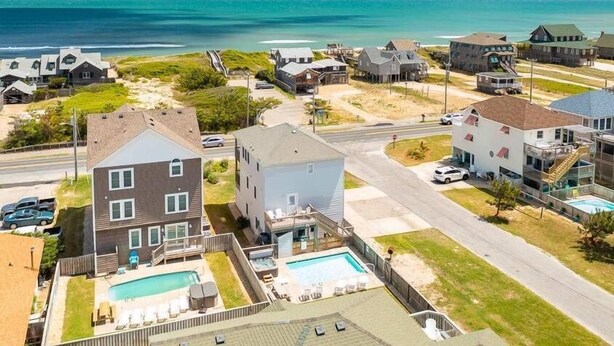Un quartier résidentiel en bord de mer, avec des maisons, une piscine et une plage en arrière-plan.