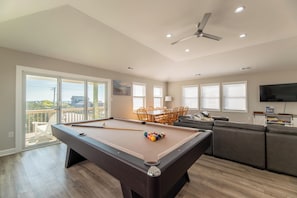Une table de billard avec des queues et des billes, un canapé, un téléviseur et un balcon aménagé avec du mobilier d’extérieur.