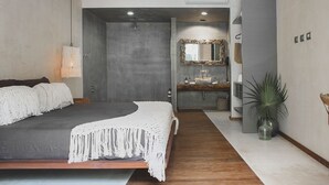 A modern bedroom with a large bed, a bathroom with a vanity, and a plant. - Cozy Rooms to let (Tulum)