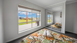 A bedroom with a large window, a bed with a floral bedspread, and a mirror reflecting the room.