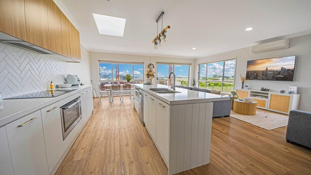A modern kitchen with a large island, wooden flooring, and a cityscape view.
