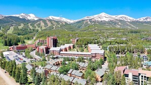 A resort with multiple buildings, including a large hotel with a central tower, surrounded by smaller structures and a parking area. - Cedars Liftside Townhome: Ski In/Ski Out (Breckenridge)