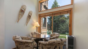 A cozy room with a round table and four patterned armchairs, a standing lamp, and a large window with a view of trees. - Cedars Liftside Townhome: Ski In/Ski Out (Breckenridge)