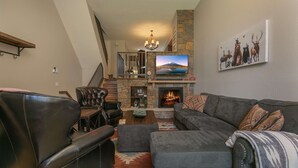 A living room with a stone fireplace, a television mounted above it, and a staircase leading to an upper level. - Cedars Liftside Townhome: Ski In/Ski Out (Breckenridge)