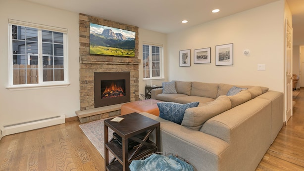 Una sala de estar con chimenea de piedra, un sofá modular grande y un televisor de pantalla plana colocado sobre la chimenea.