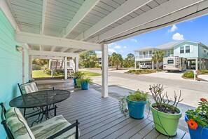 A covered porch with a table and chairs, potted plants, and a view of a street with houses and a parked RV.