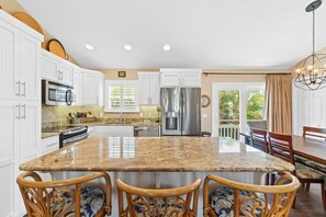 A spacious kitchen with white cabinets, a granite island, and a dining area with wooden chairs.