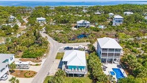 An aerial view of a coastal residential area with houses, a road, and a swimming pool.
