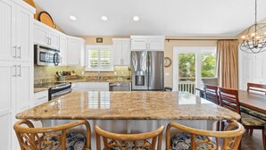 A spacious kitchen with white cabinets, a granite island, and a dining area with wooden chairs.