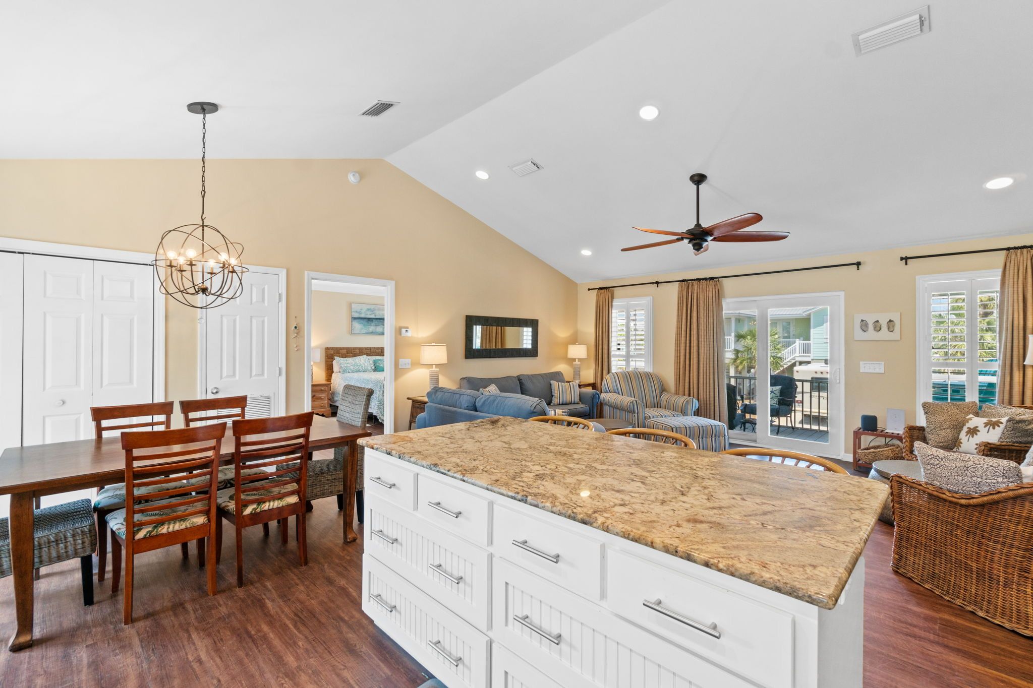 A spacious kitchen with a large island, dining area with chairs, and a living room with sofas and a ceiling fan.