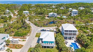An aerial view of a coastal residential area with houses, a road, and a swimming pool.