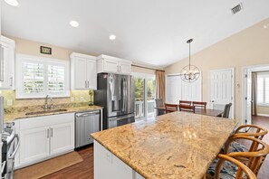 A kitchen with white cabinets, a stainless steel refrigerator, a granite countertop, and a dining area with a table and chairs.