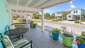 A covered porch with a table and chairs, potted plants, and a view of a street with houses and a parked RV.