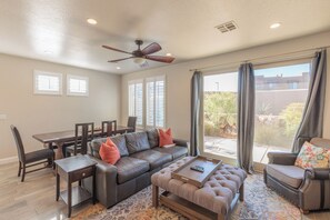 A spacious living room with a dark leather sofa, a matching ottoman, a coffee table, and a dining area with a wooden table and chairs.