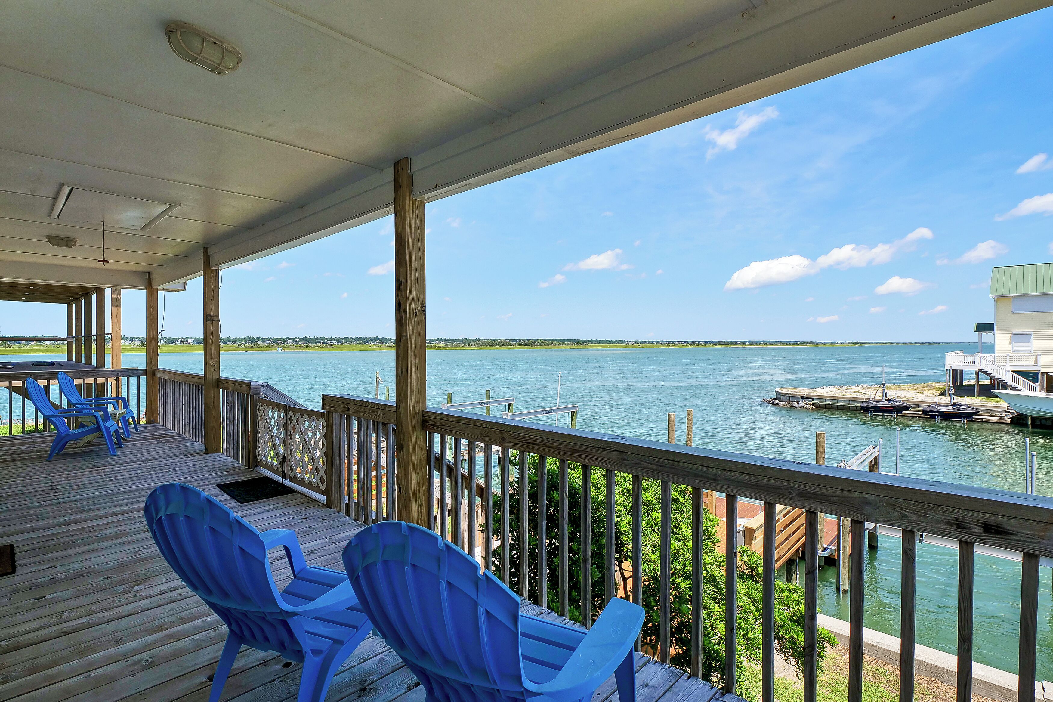 A covered deck with blue chairs and a view of the water.