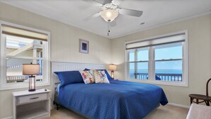 A bedroom with a bed, two bedside tables, a nightstand, a ceiling fan, and a window with a view of the ocean. - Dream On #145 - Private boat dock, short walk to the beach, dog friendly! (Topsail Beach)