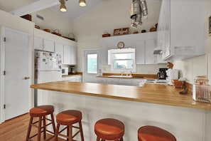 A kitchen with white cabinets, a wooden island with stools, a clock, and a window. - Dream On #145 - Private boat dock, short walk to the beach, dog friendly! (Topsail Beach)