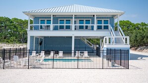 Ein Strandhaus mit zwei Etagen, einem Pool, einer überdachten Terrasse und einer Treppe, die zum oberen Stockwerk führt.