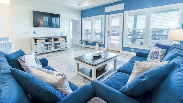 Ein geräumiges Wohnzimmer mit blauen Sofas, einem Couchtisch und einem an der Wand befestigten Fernseher.