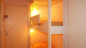 A narrow room with two bunk beds, a door, and a light fixture.