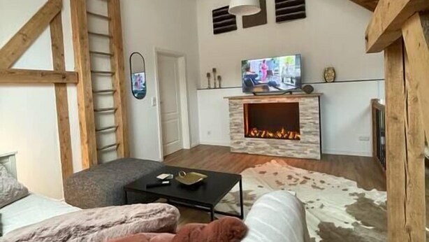 Un interior rústic amb bigues de fusta al descobert, una llar de foc, un televisor i un sofà.