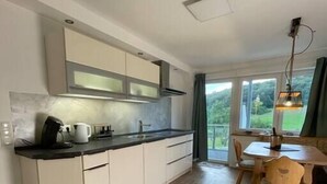 Una cuina moderna amb armaris blancs, un taulell negre i una zona de dinar amb cadires i taula de fusta.