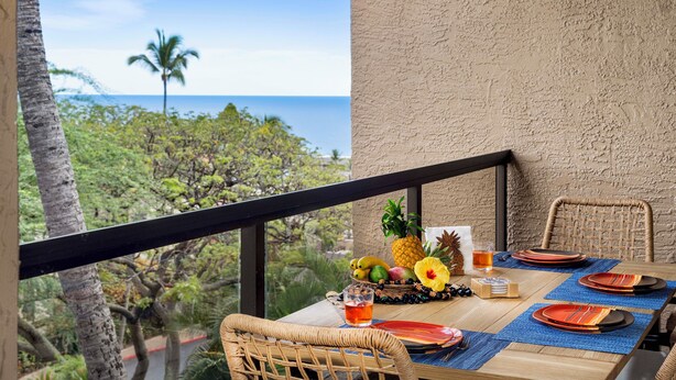 Ein Esstisch gedeckt mit Tellern, Besteck und tropischen Früchten, mit Blick auf eine üppige Landschaft und das Meer.